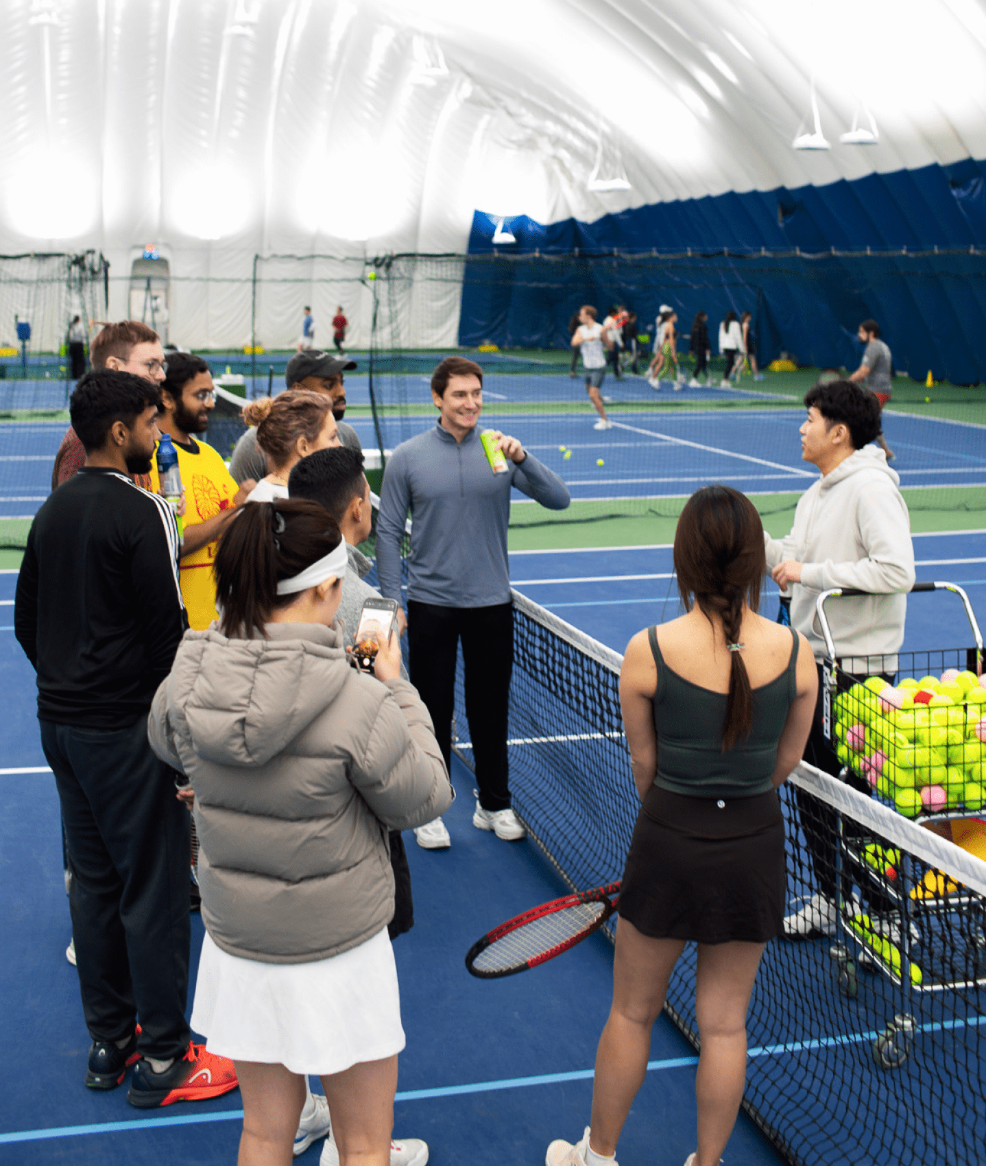 A group of NYC adults learning to play tennis on an indoor court.