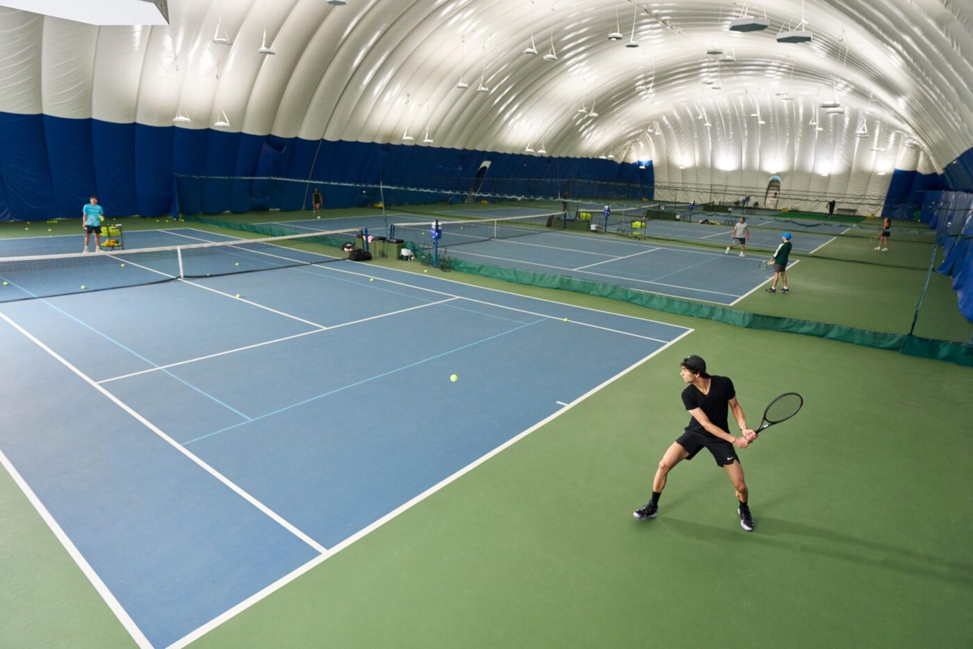 Coaches help aspiring players get better at tennis and maintain fitness across a series of four indoor courts.