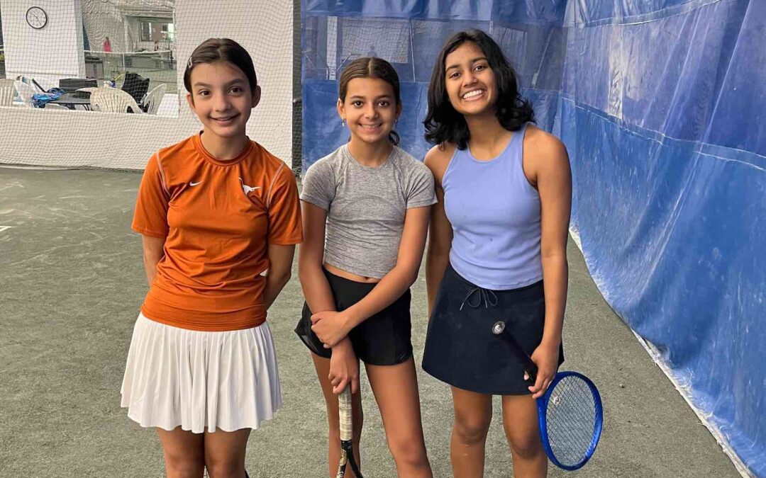 Three adolescent tennis players smiling and holding their rackets.
