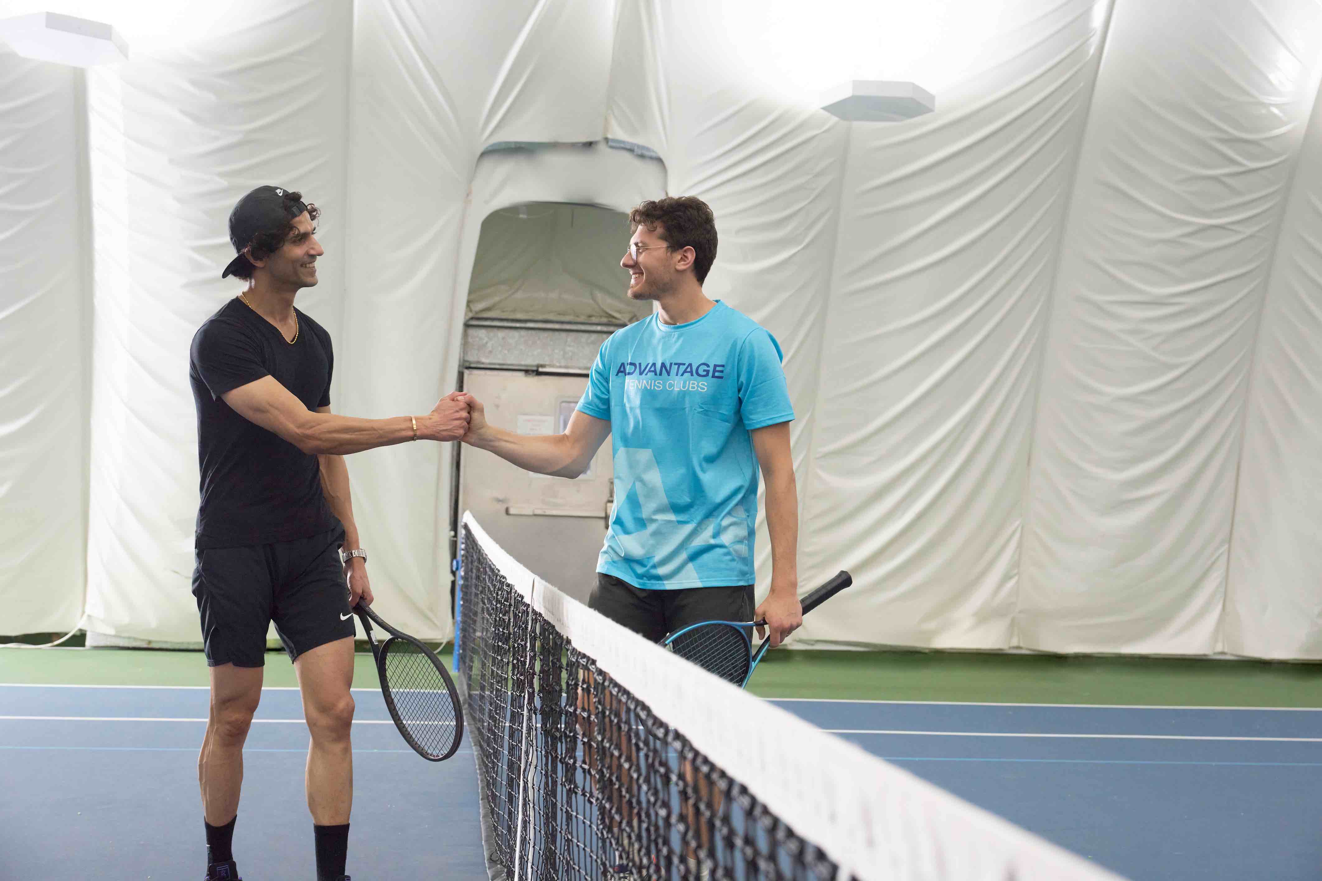 A coach and player bumping fists over the net after a beginner tennis lesson for adults.