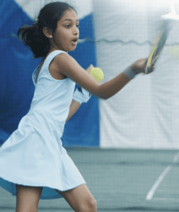 A youth athlete practicing her swing during instructional tennis lessons.