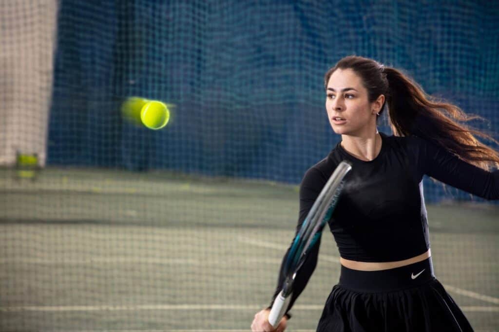 A female tennis player mid-swing at an indoor summer program.